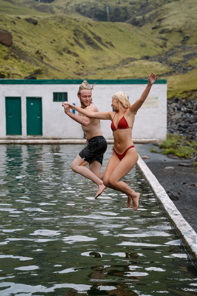 Couple splashing and laughing together in a natural hot spring during their hot springs elopement in Iceland