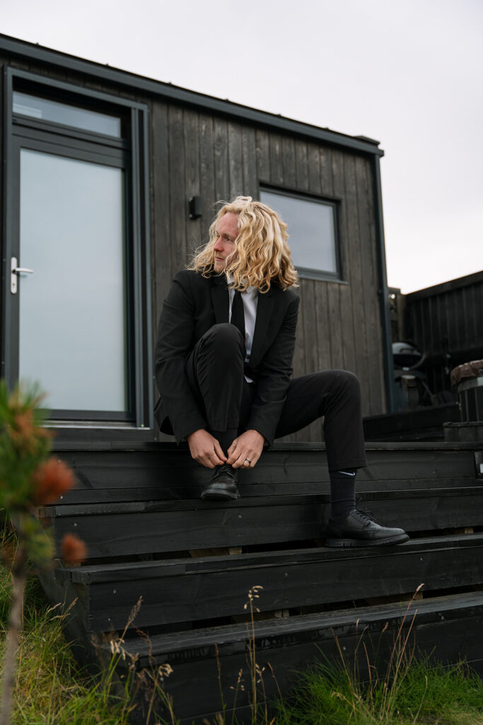 Groom adjusting his shoes at sunrise outside the glass lodge