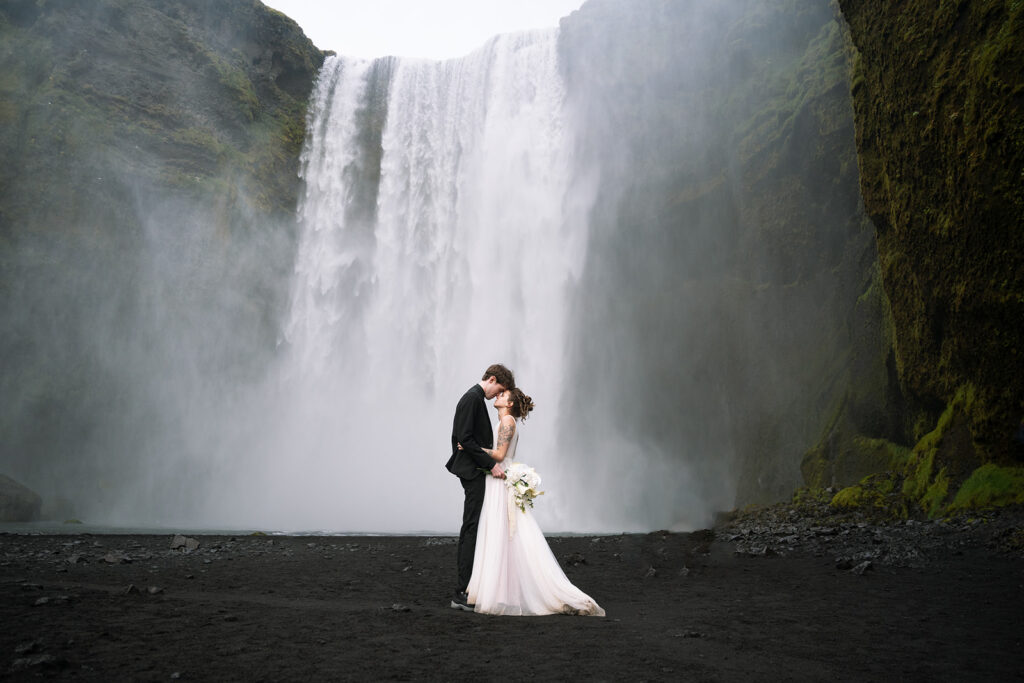 bride and groom kiss at the base of the Skogasfoss waterfall in iceland