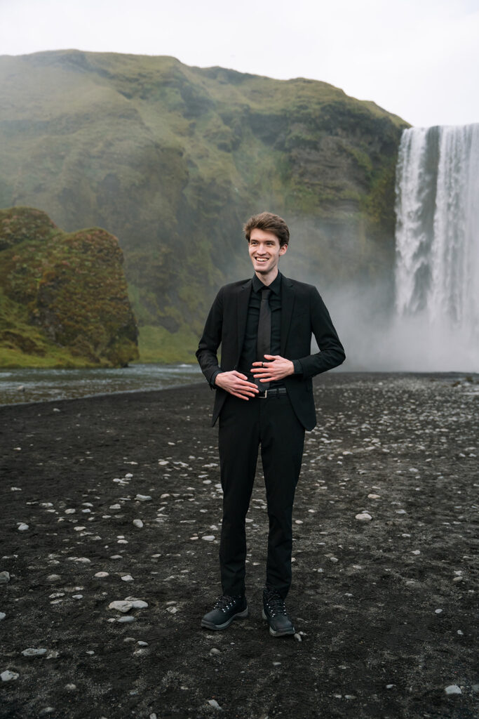 groom adjusts his suit at Skogasfoss waterfall