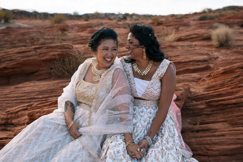 Joyful same-sex couple sitting close on red rock during their inclusive Utah elopement