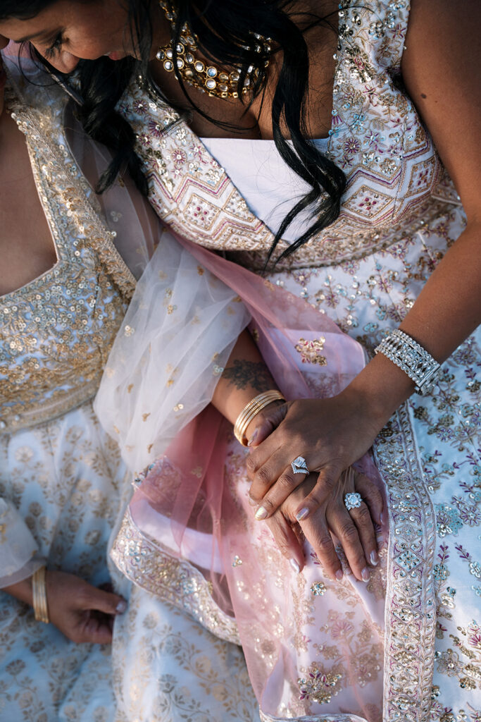 Detail shot of two brides’ hands and wedding rings during an intimate desert ceremony.